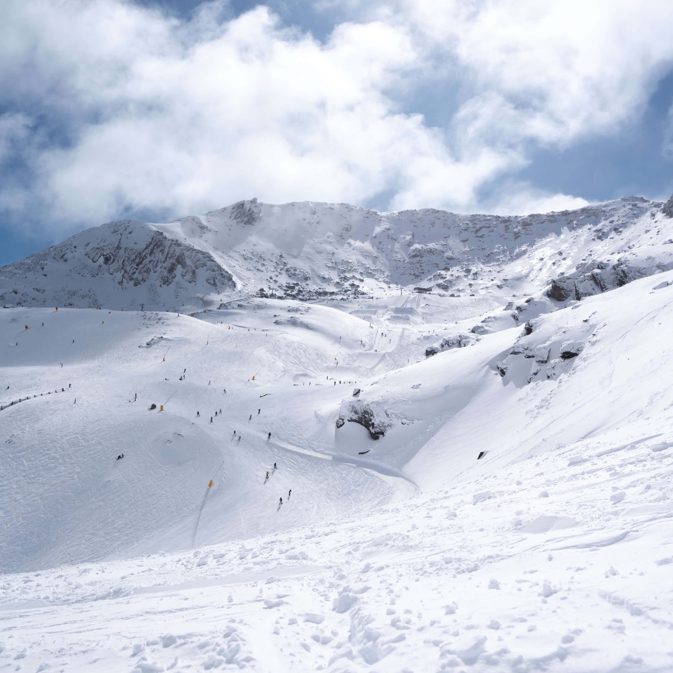 Skiers descending snowy mountain slopes under a partly cloudy sky.